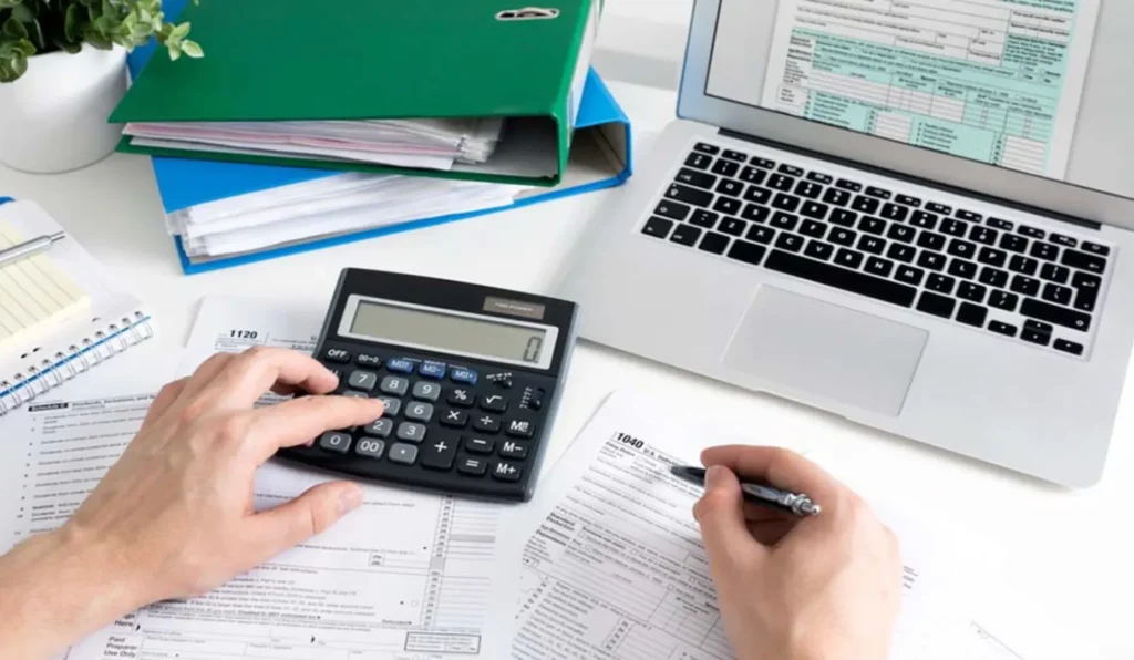 hand on calculator with pen and laptop