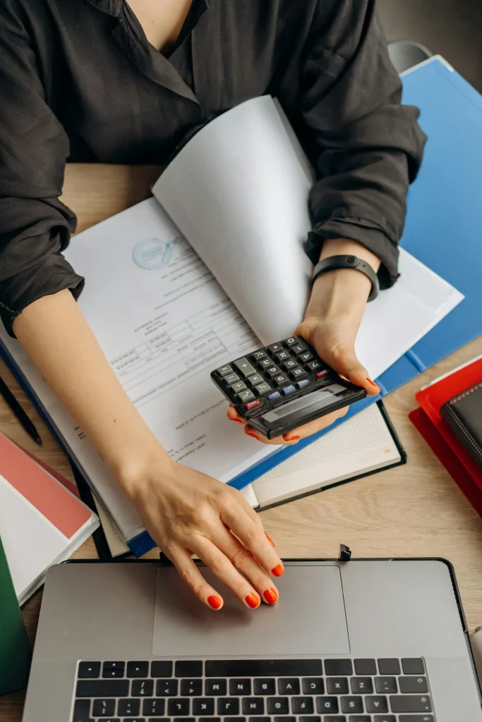 Bookkeeper scrolling on laptop with calculator in other hand